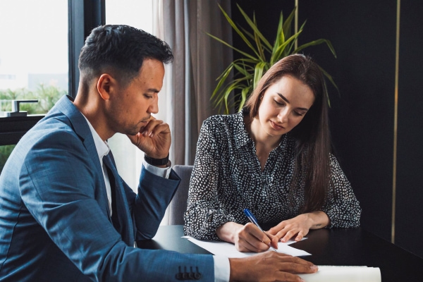 a person and person sitting at a table writing on paper